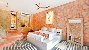 A bedroom with a large bed, a ceiling fan, stone walls, and a patterned floor.