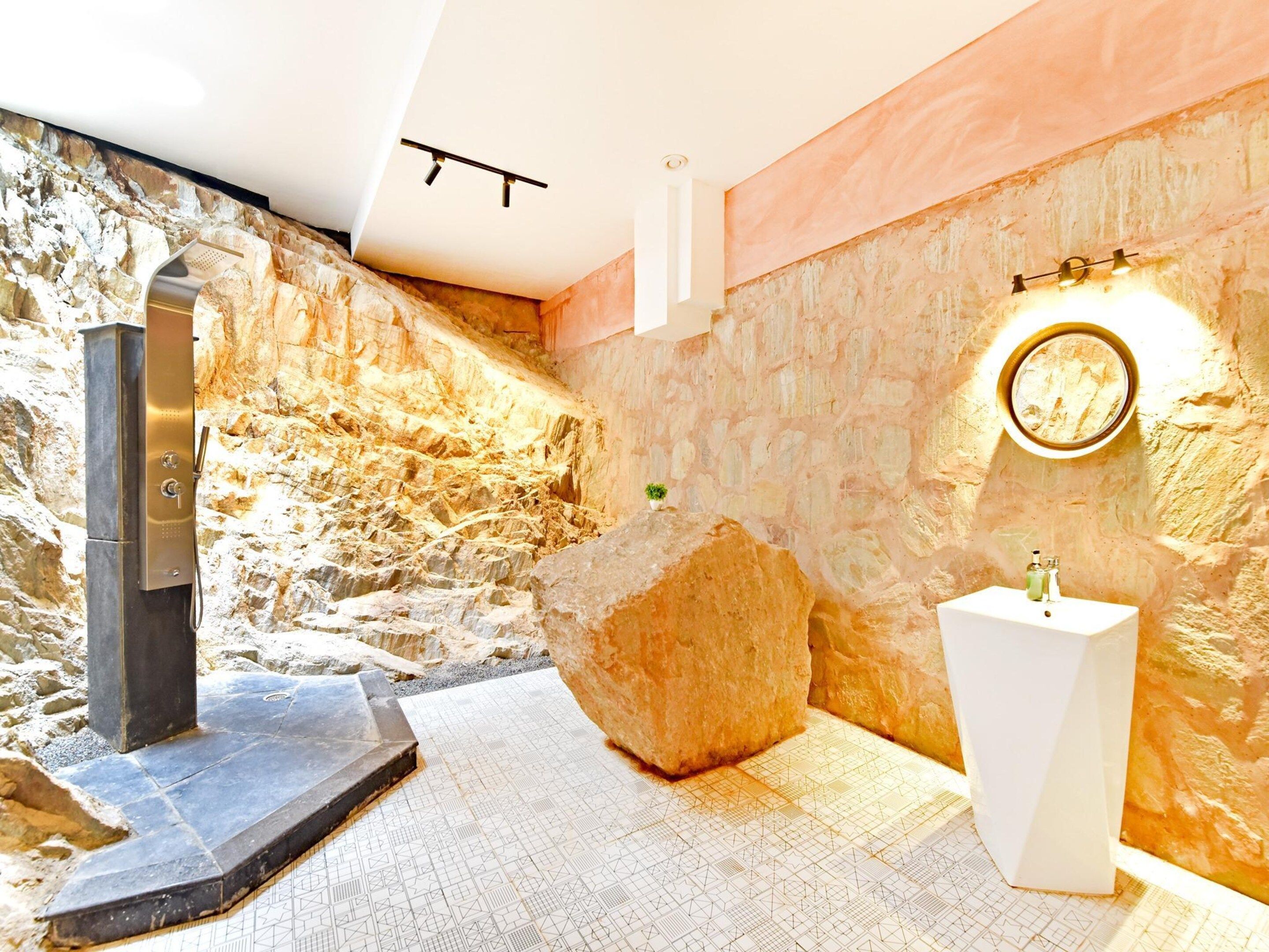 A bathroom with a stone wall, a large rock, a modern sink, and a wall-mounted light fixture.