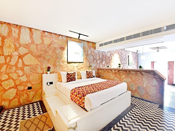 Habitación de hotel con pared de piedra, cama con ropa de cama estampada, una mesita y vistas al exterior.