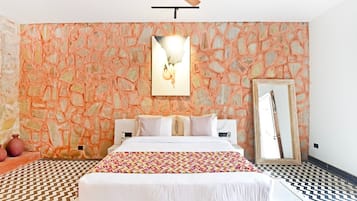 Un dormitorio con una cama, un ventilador de techo, una pared con diseño de piedra, un espejo y un piso estampado.