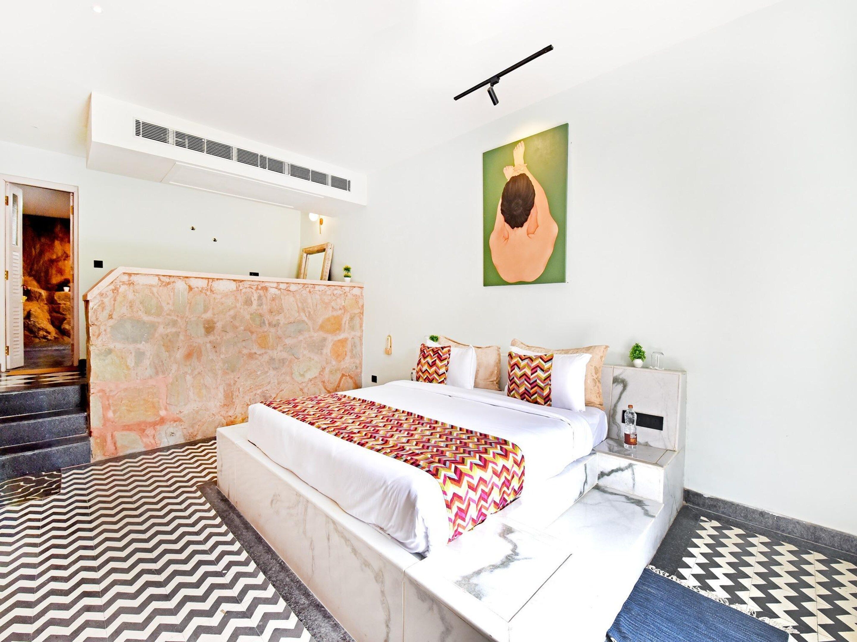 A hotel room with a bed, a stone accent wall, a painting, and a patterned rug.