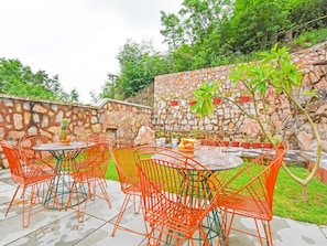 An outdoor seating area with stone walls and greenery. - Dancenter Parijat 4bhk Pvt Villa I Pool I Udaipur (Udaipur)