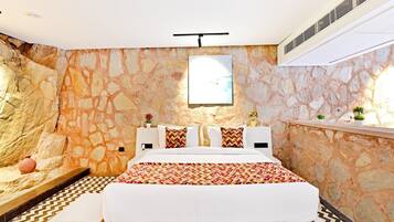 Quarto com parede de pedra, cama com roupa de cama branca, manta estampada e uma pequena planta em vaso no criado-mudo.