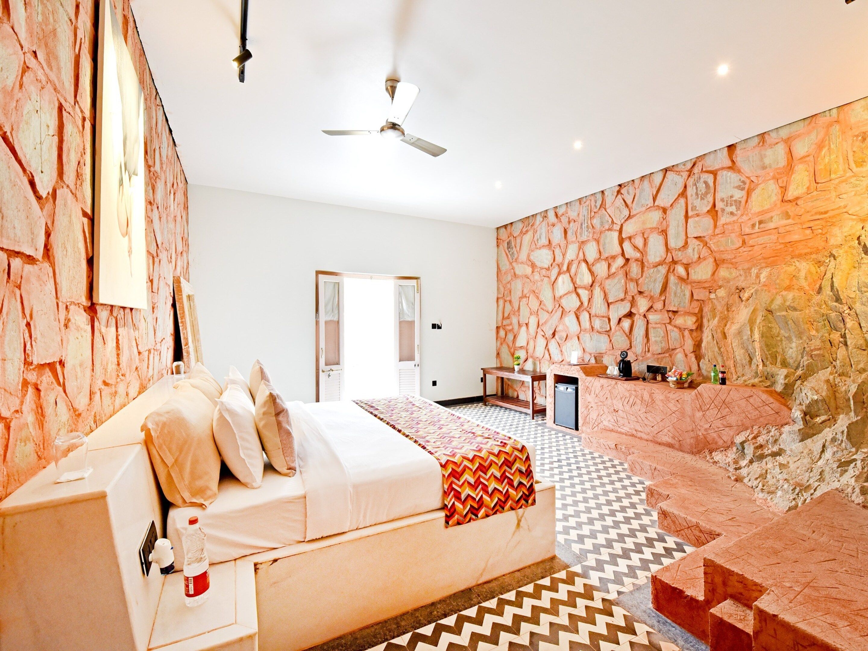 A bedroom with a bed, a desk, and a stone wall.