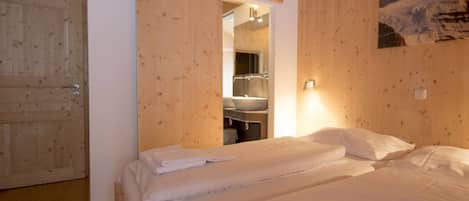 Habitación de hotel con dos camas, paredes de madera, un baño con lavamanos y una puerta.