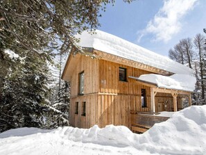 Una cabaña de madera con techo nevado, rodeada de árboles y un paisaje invernal.