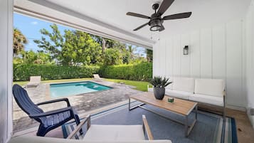 A modern outdoor patio with a pool, lounge chairs, a sofa, and a ceiling fan.