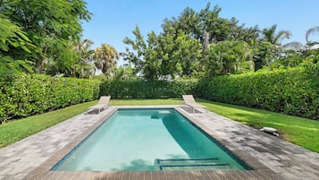 Ein rechteckiger Pool mit gefliestem Sonnendeck, umgeben von üppiger Vegetation und Palmen.