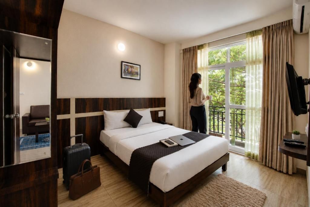 Ein Hotelzimmer mit Bett, Schreibtisch, Stuhl, Koffer und einem Balkon mit Vorhängen.