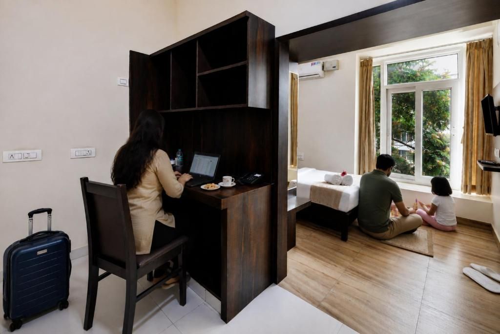 Ein Zimmer mit Schreibtisch, Stuhl, Bett, Fenster und Koffer.