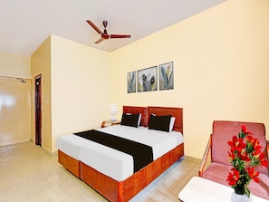 A hotel room with a bed, a ceiling fan, a chair, and a vase with flowers. - Premium Hotel sbt (Visakhapatnam)