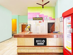 A hotel reception desk with a reception sign, a clock, a no-smoking sign, and a refrigerator with beverages. - Premium Hotel sbt (Visakhapatnam)