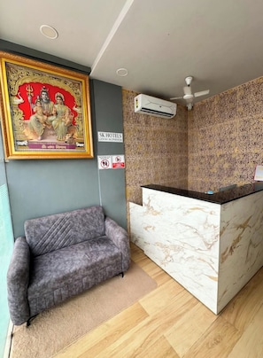 A hotel reception area with a marble counter, a grey sofa, and a wall-mounted air conditioner.