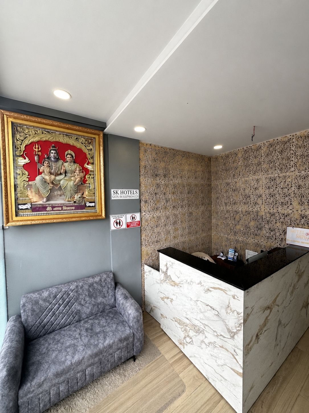 A hotel reception area with a marble counter, a framed religious painting, a sofa, and a patterned wall.