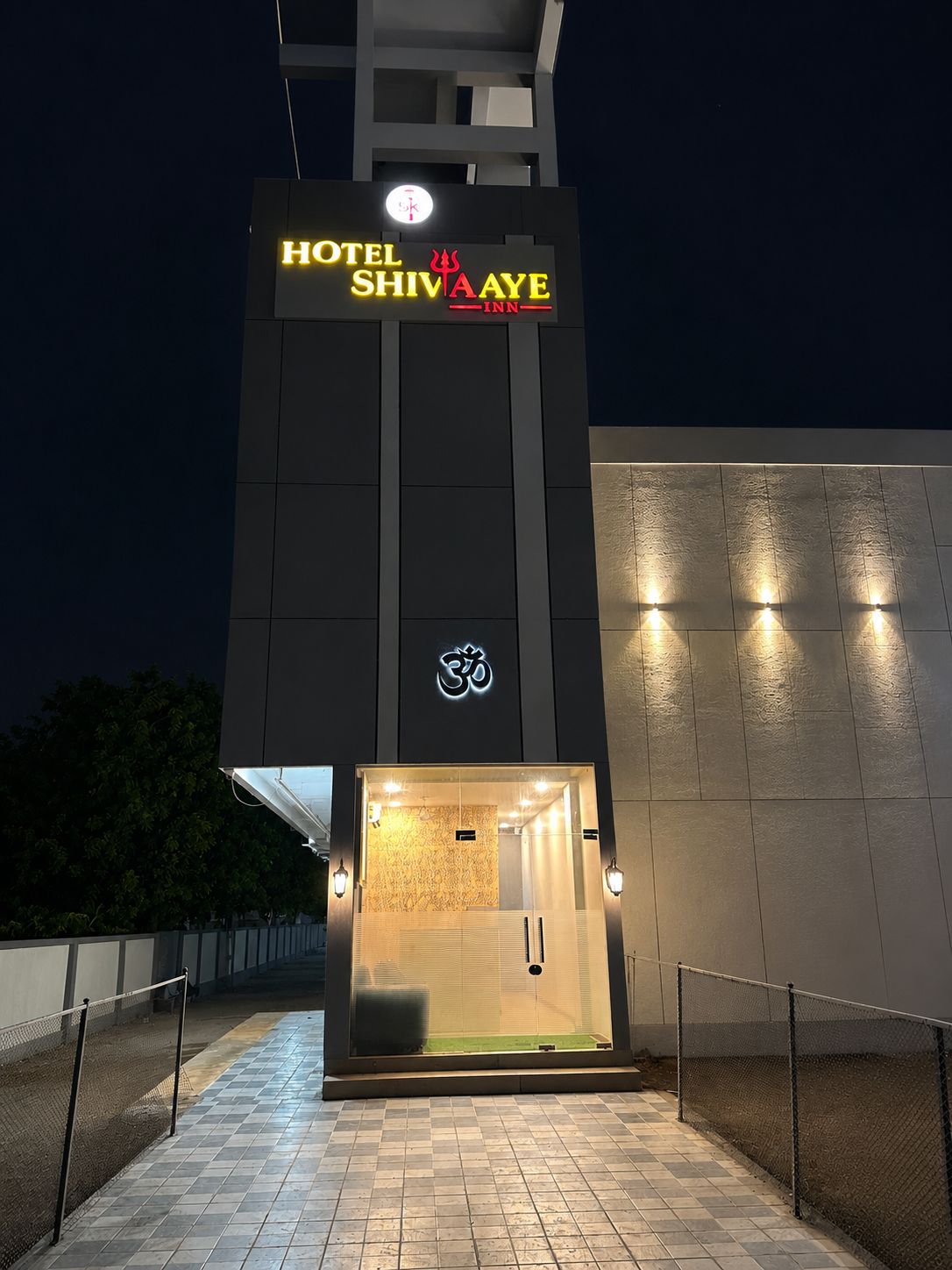 A hotel entrance with a sign reading 'HOTEL SHIVA AYE INN' and a symbol above the door.