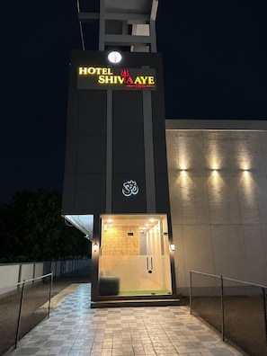 Entrada de un hotel con un cartel que dice 'HOTEL SHIVA AYE INN' y un símbolo sobre la puerta.