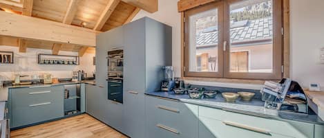 Una cocina moderna con armarios grises, un horno empotrado y una ventana con vistas a un paisaje montañoso.