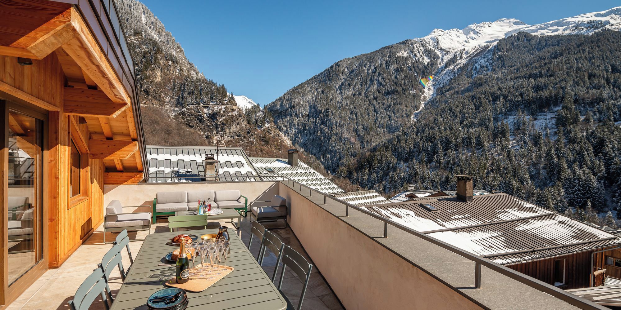 Un bâtiment moderne avec une façade en bois et une terrasse dotée d’un espace salon extérieur et d’une table dressée pour les repas.