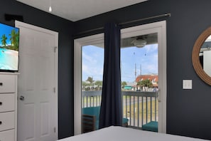 Ein Zimmer mit Bett, Fernseher auf einer Kommode, einem Balkon mit Blick auf die Straße und Gebäude sowie einer Tür zu einem weiteren Raum.