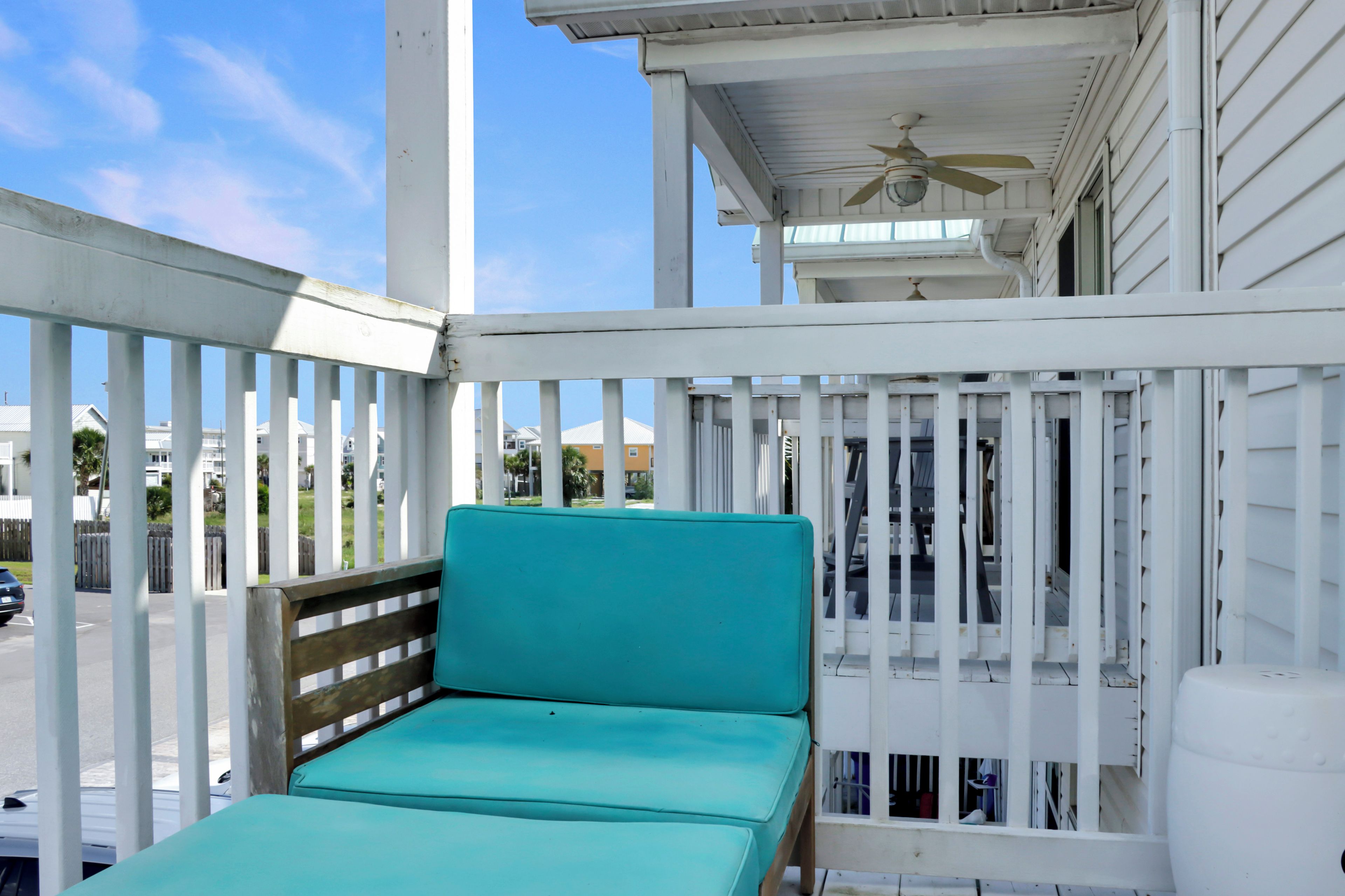 A turquoise chair on a white porch with a ceiling fan.