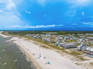 Eine Wohngegend an der Küste mit Häusern direkt am Strand, einem Sandstrand und blauem Himmel.