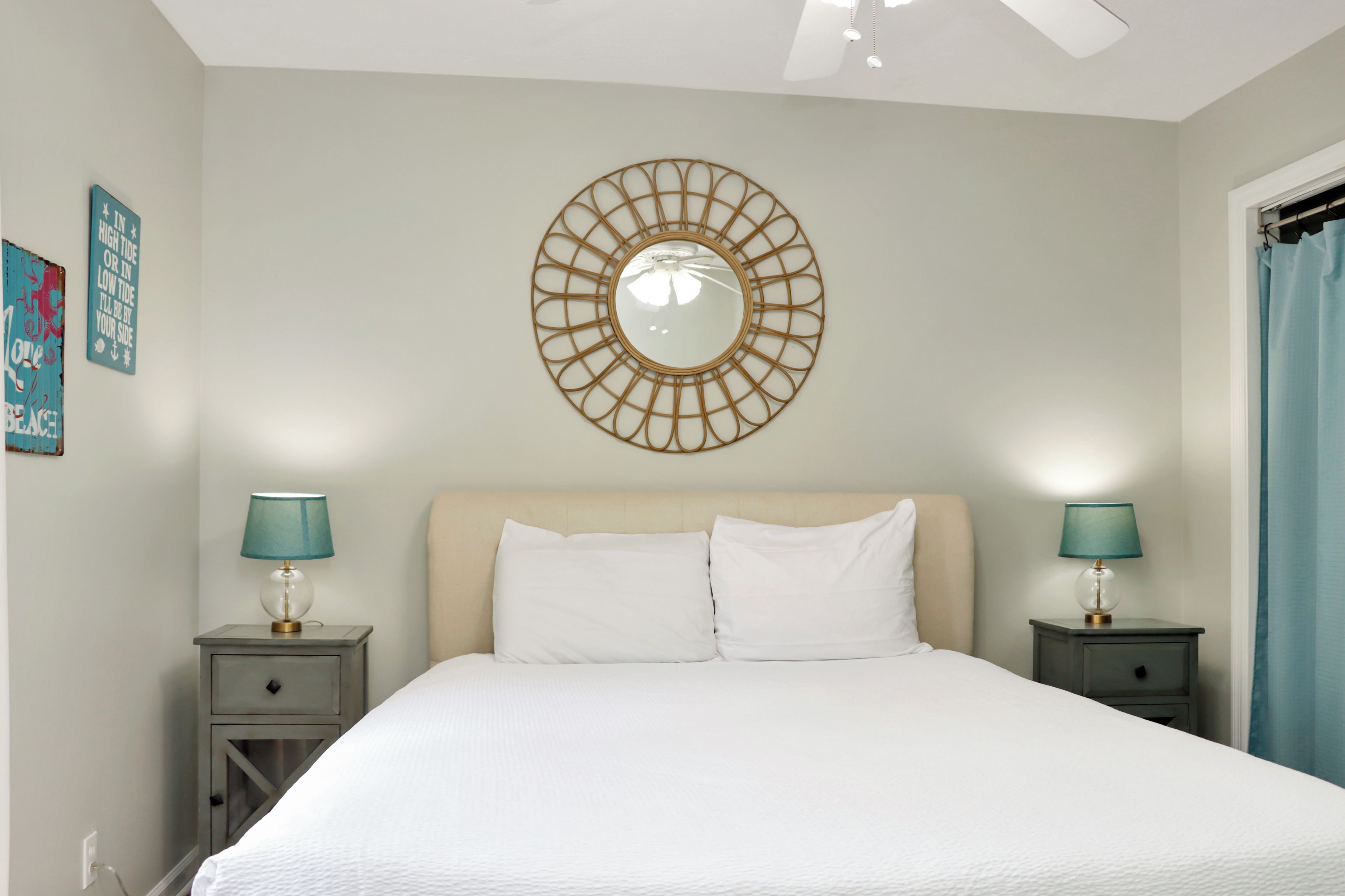A bedroom with a large bed, two bedside tables with lamps, a wall-mounted mirror, and a window with curtains.