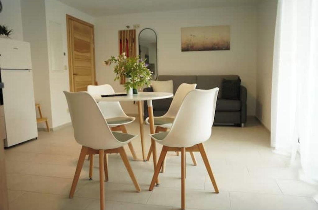 Uma sala de jantar com uma mesa redonda e quatro cadeiras, um sofá, um espelho e um quadro na parede.