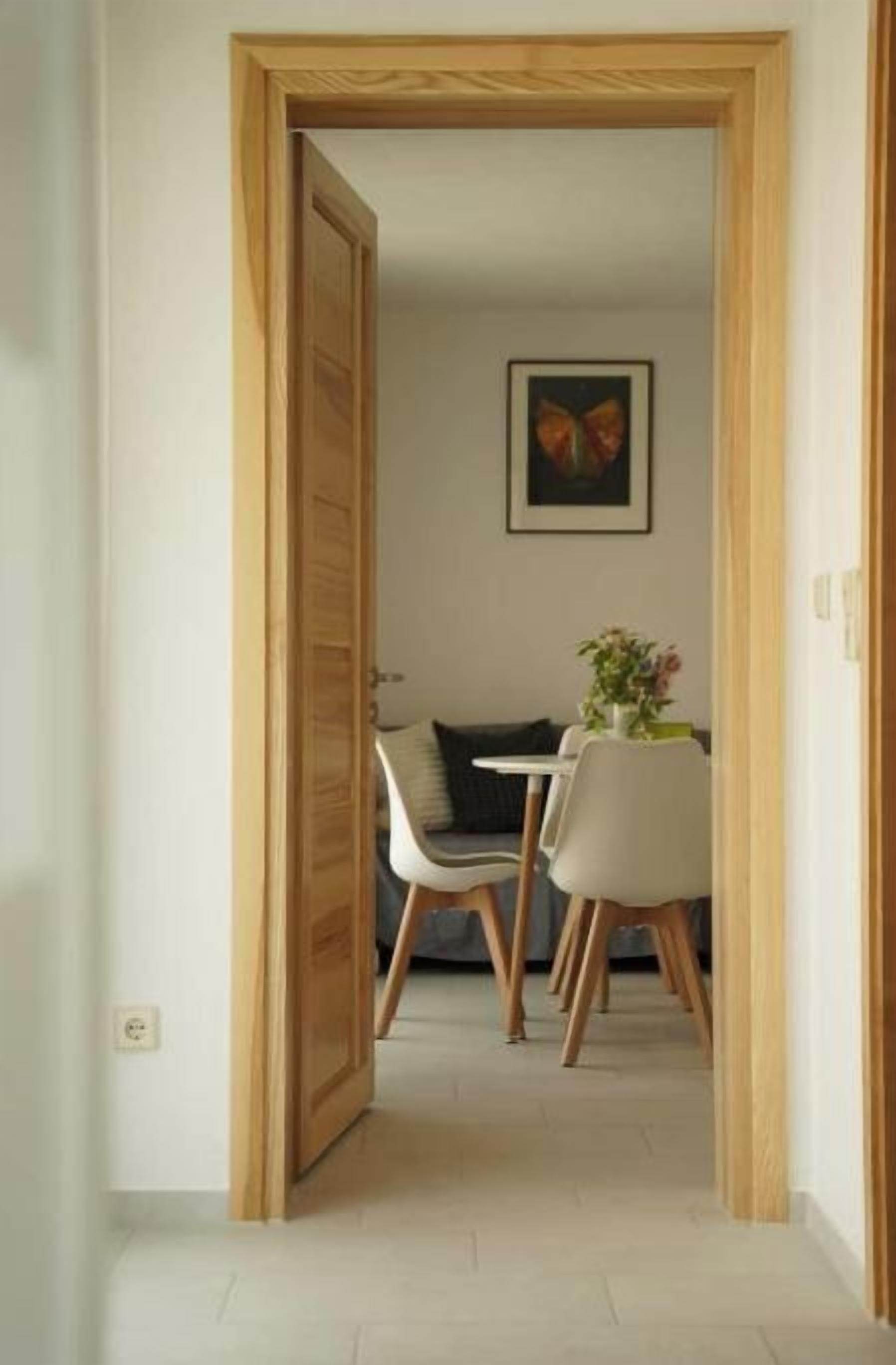 Un couloir mène à une salle à manger où se trouvent une table et des chaises, un tableau encadré au mur et une porte sur la gauche.