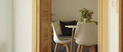 Un couloir mène à une salle à manger où se trouvent une table et des chaises, un tableau encadré au mur et une porte sur la gauche.