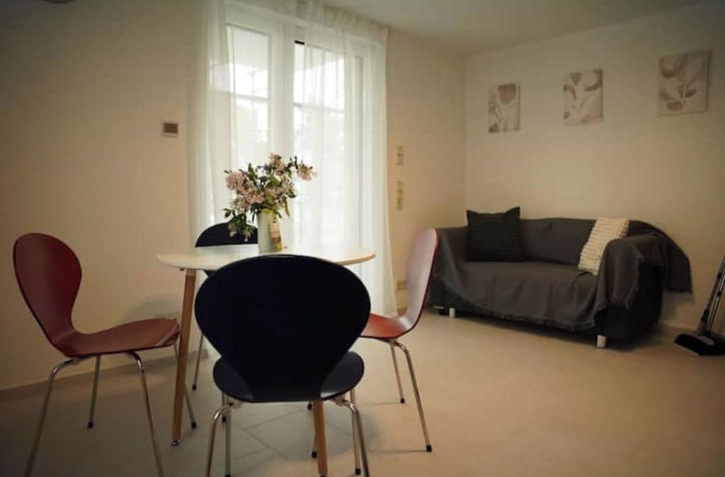 Ein Wohnzimmer mit einer Couch, zwei Sesseln, einem Tisch und einer Blumenvase.