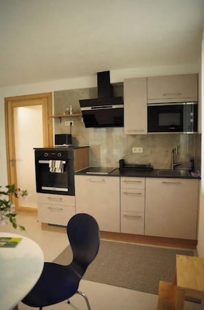 A compact kitchen with a microwave, oven, and gas stove. There is a dining area with a table and chairs. - Standard Apartment (Reutlingen)
