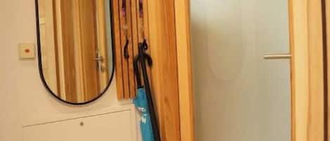 Une pièce avec une porte en bois, un miroir et un porte-manteau sur lequel est posé un vêtement bleu.