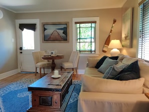 A living room with a sofa, a coffee table, two chairs, a painting, and a window with blinds. - Jackson's Cottage Retreat near Sony Studios (Culver City)