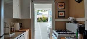 Cocina compacta con armarios blancos, estufa a gas y cafetera. Hay dos cuadros en la pared, uno con cerezas y otro con manzanas.