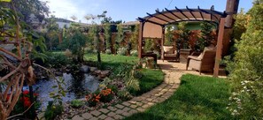 Ein Garten mit Teich, einer Pergola und Gartenmöbeln.