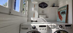 A laundry room with two washing machines, a drying rack, and a sign indicating self-service laundry available 24 hours. - Jackson's Cottage Retreat near Sony Studios (Culver City)