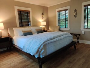 A bedroom with a large bed, two bedside lamps, a chair, and a window with blinds. - Jackson's Cottage Retreat near Sony Studios (Culver City)