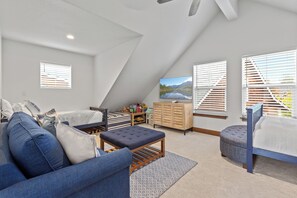 Ein Schlafzimmer mit schrägen Wänden, einem Bett, einer Schlafcouch, einem Fernseher und einem Fenster mit Jalousien.