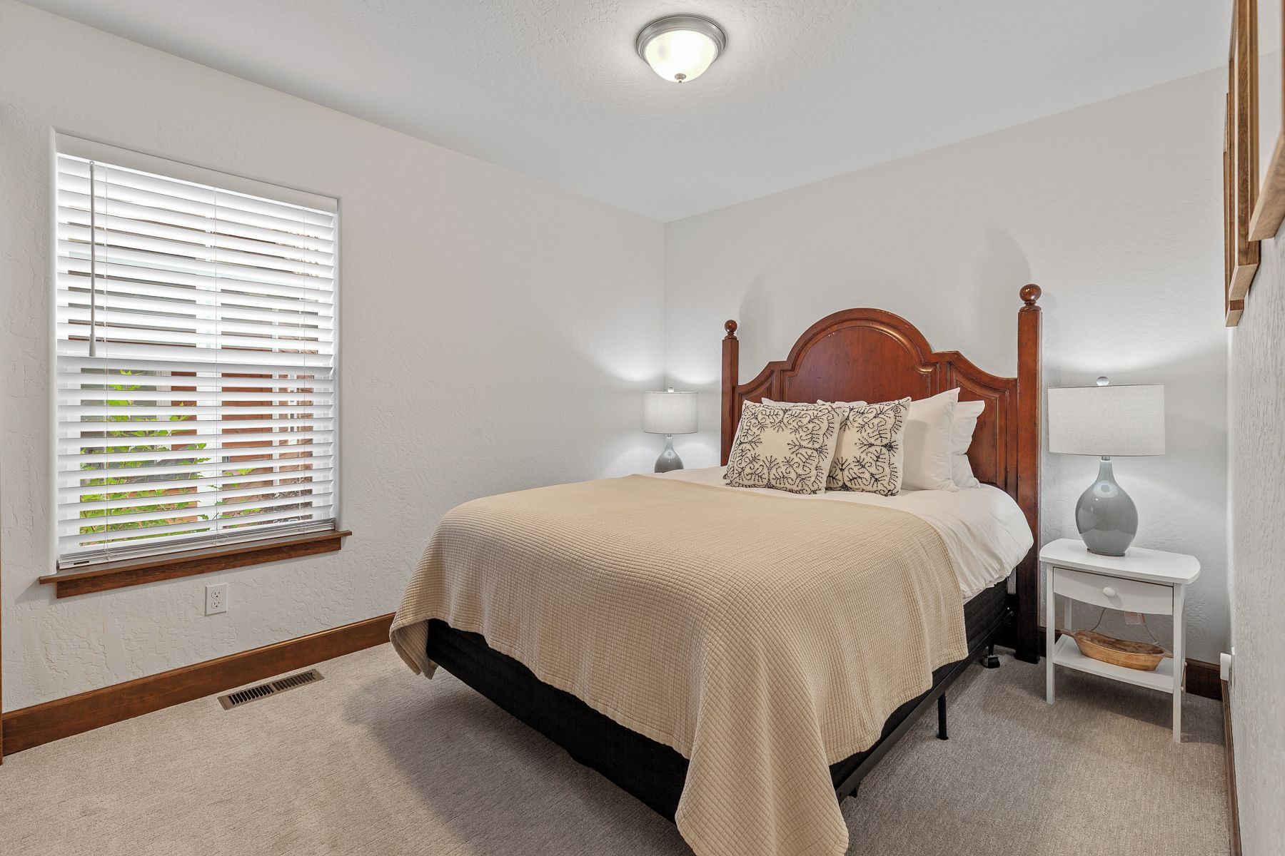 A bedroom with a four-poster bed, bedside tables, and a window with blinds.