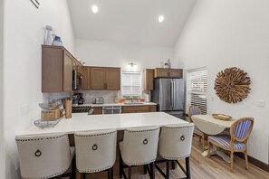 A kitchen with wooden cabinets, a stainless steel refrigerator, and a dining area with a table and chairs. - New! Cottage by the Bay | 3 Min Walk To Dover Bay Marina | Pet Friendly | AC (Dover)