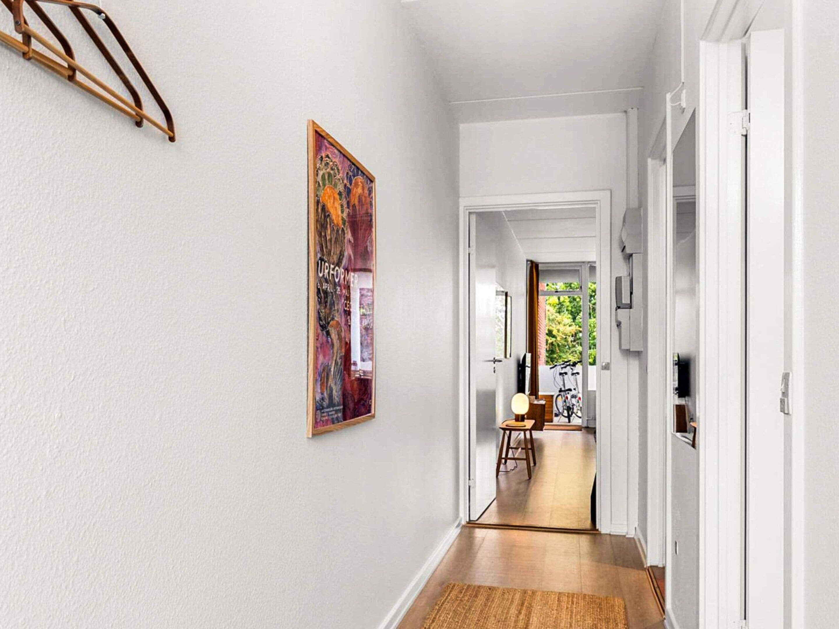 A hallway with a wooden floor, a door leading to another room, and a framed artwork on the wall.
