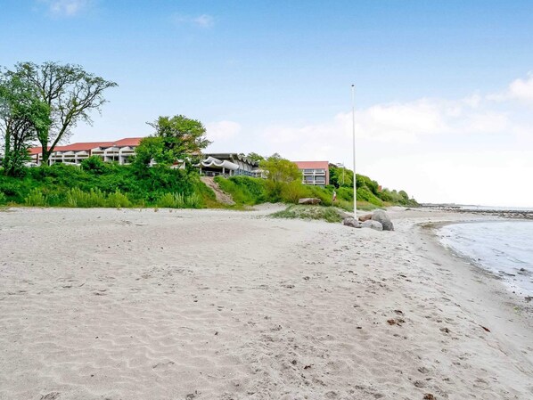 A sandy beach with a building in the background. - 4 Star Holiday Home in Faaborg (Faaborg)