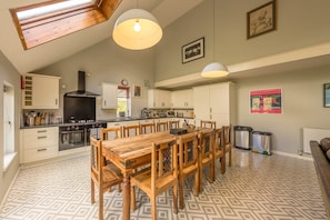 A spacious kitchen with a dining area, featuring a large wooden table and chairs, a built-in oven, and pendant lighting.
