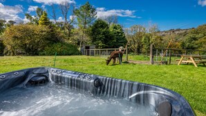 A hot tub in a grassy area with a wooden fence and trees in the background. - Pet Friendly Farm Stay with Hot Tub Pembrokeshire | Clematis-Y-Ffynnon (Pembrokeshire)