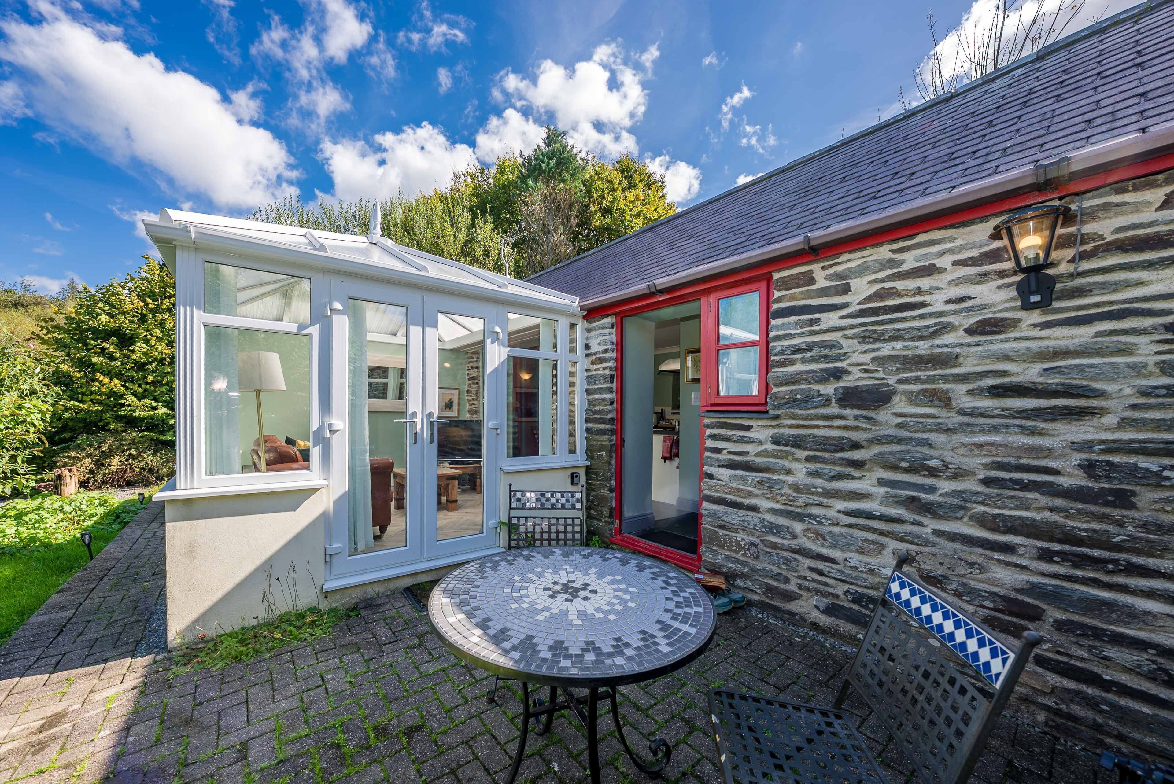 A stone building with a glass conservatory and a tiled patio.