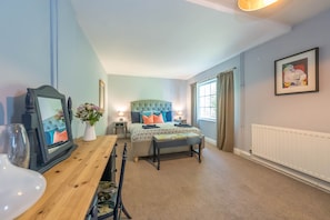 A bedroom with a bed, bedside tables, a mirror, a window with curtains, and a radiator. - Romantic stone cottage with hot tub in Pembrokeshire | Eiddew-Y-Ffynnon (Pembrokeshire)