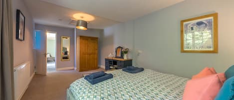 A bedroom with a bed, a dresser, a mirror, and a door leading to another room.