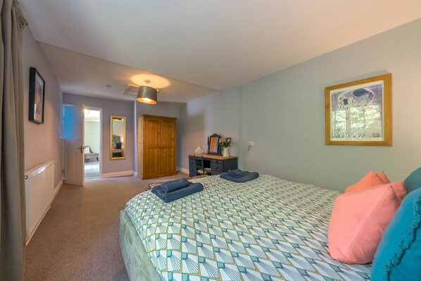 A bedroom with a bed, a dresser, a mirror, and a door leading to another room.