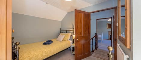 A bedroom with a single bed, a nightstand, a lamp, and a door leading to a staircase.