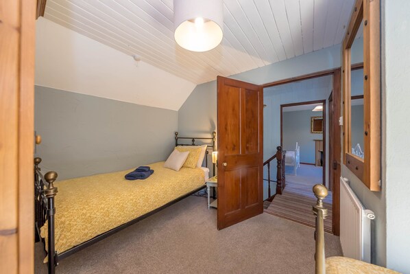 A bedroom with a single bed, a nightstand, a lamp, and a door leading to a staircase.